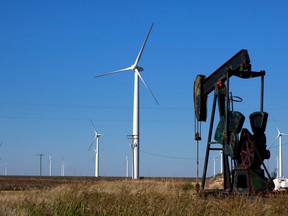 Wind turbines stand next to an oil pumpjack in a field.