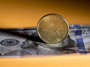 A Canadian one dollar coin, also known as a Loonie, and a U.S. one hundred dollar banknote