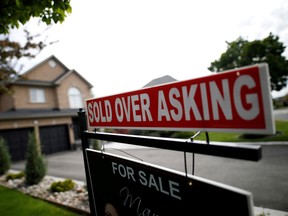 A real estate sign that reads "For Sale" and "Sold Above Asking" stands in front of housing in Vaughan, Ont.