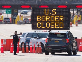 In this file photo taken on March 22, 2020 US Customs officers speaks with people in a car beside a sign saying that the US border is closed at the US/Canada border in Lansdowne, Ontario