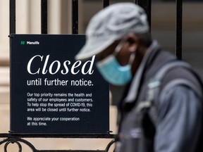A pedestrian wearing a mask walks past a closed sign on the front gates of Manulife’s headquarters in Toronto last week. The third wave has kept Ontario in lockdown.