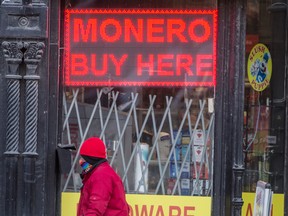 A pedestrian wearing a mask walks past a digital sign for Monero on Toronto’s Yonge Street. The digital currency is becoming popular with ransomware gangs because it is designed to obscure the sender and receiver, as well as the amount exchanged.