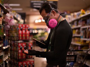 Instacart employee Eric Cohn, 34, uses his phone to scan an item for a delivery order he is preparing from Fry's grocery store while wearing a respirator mask to help protect himself and slow the spread of the coronavirus disease (COVID-19) in Tucson, Arizona, U.S., April 4, 2020.