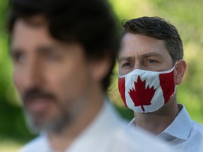 Liberal MP William Amos, right, wearing a Canadian flag mask, stands behind Prime Minister Justin Trudeau as he speaks during a news conference in Chelsea , Que. Amos has had two parliamentary video gaffes.