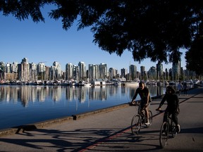 People ride bicycles in front of yachts and boats moored at Coal Harbour marina in Vancouver, British Columbia.