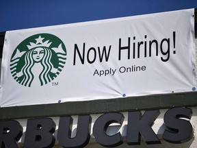 A "Now Hiring" sign is displayed outside a Starbucks drive-thru coffee shop.