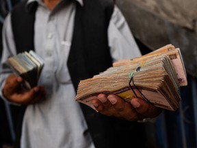 A man holds a bundles of Afghan afghani banknotes at the main money exchange market in Kabul, Afghanistan, on Thursday, July 12, 2018.