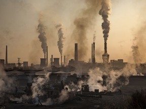 Smoke billows from a large steel plant as a Chinese labourer works at a  steel factory, foreground  in Inner Mongolia, China.