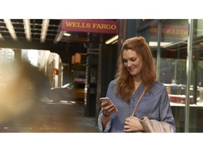 A woman looks at her phone with Wells Fargo sign in background.