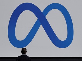 A man stands in front of a sign of Meta, the new name for the company formerly known as Facebook, at its headquarters in Menlo Park, California.
