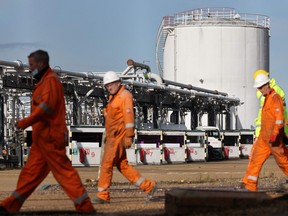 A tanker is stocked with fuel as workers walk past at the Hamble oil refinery near Southampton, southern England on Oct. 4, 2021.