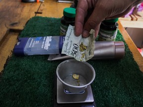 A customer places gold flakes wrapped in a crumpled bolivar banknote on to a scale for payment at a pharmacy in Tumeremo, Bolivar state, Venezuela,