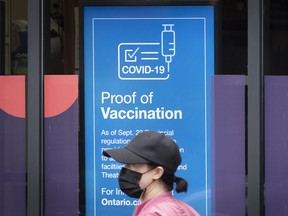A person wearing a mask walks past information about COVID-19 vaccination proof in Kingston, Ont. on Sept. 23, 2021.