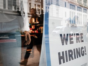 People walk by a hiring sign in a window along a main shopping street in Manhattan on Nov. 17, 2021 in New York City.