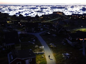 A pedestrian walks at dusk as ice and icebergs float in Disko Bay on Sept. 2, 2021 in Ilulissat, Greenland.