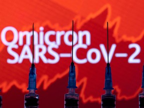 Syringes with needles are seen in front of a displayed stock graph and words "Omicron SARS-CoV-2".