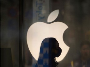 A employee wearing a protective mask is silhouetted while standing in front of an Apple Inc. logo at a store in Japan.