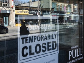 Storefronts in Ottawa's Glebe neighbourhood are reflected in a sign indicating the temporary closure of a business to prevent the spread of COVID-19.