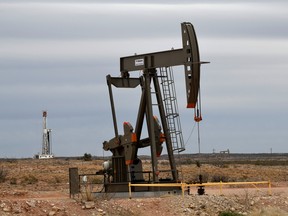 A pumpjack operates in front of a drilling rig owned by Exxon near Carlsbad, New Mexico.