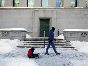 Un résident tire un enfant dans un traîneau devant l'édifice de la Banque du Canada à Ottawa, mardi.