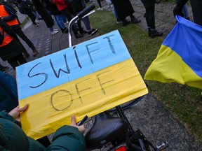 Ein Demonstrant hält ein Plakat mit der Aufschrift „SWIFT OFF“, das sich auf das internationale SWIFT-Finanztransfernetzwerk bezieht, während eines Protests gegen Russlands Invasion in der Ukraine am 25. Februar 2022 vor dem Kanzleramt in Berlin.