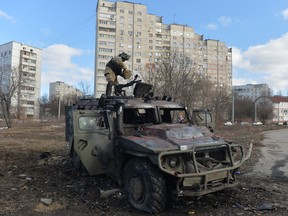 An Ukrainian Territorial Defence fighter examines a destroyed Russian infantry mobility vehicle GAZ Tigr after the fight in Kharkiv on Sunday. Russian artillery bombarded residential districts of Ukraine's second largest city today, killing possibly dozens of people, Ukrainian officials said.