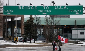 People walk with Canadian flags as truckers and supporters continue blocking access to the Ambassador Bridge on Friday.