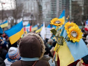 A person holds sunflowers and a Ukrainian flag as members of the Ukrainian community protest at Place du Canada in Montreal.