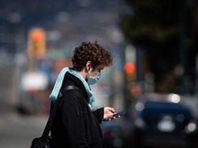 A man wearing a protective face mask looks at his phone while walking in the Downtown Eastside of Vancouver.