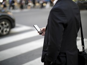 A pedestrian looks at a smartphone while standing at a corner in the financial district of Toronto.