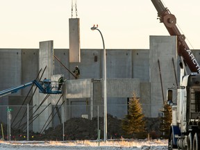 A crane swings a precast concrete wall panel into place on a new industrial building under construction.