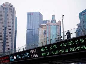 A man stands on an overpass with an electronic board showing Shanghai and Shenzhen stock indexes at the Lujiazui financial district in Shanghai, China.