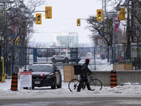 A cyclist pushes his bike across an intersection past temporary fencing as police watch from their car on Feb. 23, 2022 in Ottawa.