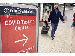Passengers pass a sign for a coronavirus testing centre at London Luton Airport in Luton, U.K., on Monday, Jan. 10, 2022. The U.K. will no longer require vaccinated travelers to take a Covid-19 test before boarding a flight to the country, after airlines hard-hit by the omicron variant lobbied for the rules to be eased.