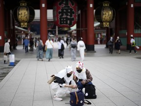 Foreign tourists wearing protective masks to help curb the spread of the coronavirus take a selfie at a shopping street at the Asakusa district Friday, June 10, 2022, in Tokyo. Japan on Friday eased its borders for foreign tourists and began accepting applications, but only for those on guided package tours who are willing to follow mask-wearing and other antivirus measures as the country cautiously tries to balance business and infection worries.