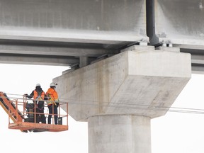 Workers are shown beneath a section of the Réseau express métropolitain (REM) a new automated light rail network in Montreal, Wednesday, February 2, 2022.
