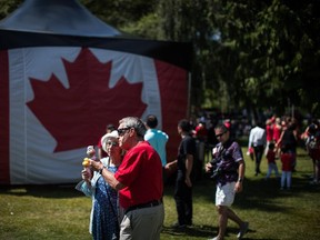 An elderly couple eat ice cream cones near a large Canadian flag during Canada Day festivities in West Vancouver on July 1, 2019.