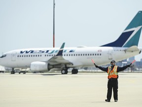 Airline groundcrew work as a grounded Westjest plane sits on the tarmac at Pearson International Airport during the during the COVID-19 pandemic in Toronto on Tuesday, April 27, 2021. The chief executive of WestJet Airlines Ltd. says it is flying 32 per cent fewer flights in and out of Toronto Pearson International Airport in July than it did in 2019.