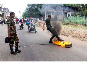 A Sri Lankan security personnel kicks a burning tire thrown by demonstrators to block a road during a protest in Colombo on June 7. Photographer: -/AFP/Getty Images