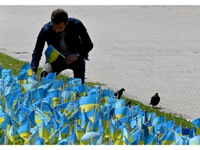 A man sticks into a grass plot small Ukrainian flags carrying the names of the Ukrainian servicemen killed in the war with Russia, in the center of Ukrainian capital of Kyiv on June 22, 2022.  Photographer: Sergei Supinsky/AFP/Getty Images
