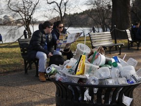 FILE - A trash can overflows as people sit outside of the Martin Luther King Jr. Memorial by the Tidal Basin, Dec. 27, 2018, in Washington, during a partial government shutdown. The Interior Department said Wednesday, June 8, 2022, it will phase out single-use plastic products on national parks and other public lands over the next decade, targeting a leading source of U.S. plastic waste such as food and beverage containers, straws and bags.