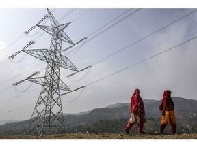 Woman walk past a Sterlite Power Transmission Ltd. transmission tower in Rajouri district, Jammu and Kashmir, India, on Thursday, Nov. 16, 2017. In Prime Minister Narendra Modi's push to supply electricity to every Indian household, connecting homes in the state of Jammu & Kashmir might be the toughest. Along India's violence-prone northern border, engineers and construction workers are electrifying one of the country's most inhospitable states.