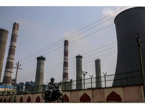 A motorcyclist drives past chimneys and a cooling tower at the coal-fired NTPC Simhadri thermal power plant in the outskirts of Visakhapatnam, Andhra Pradesh, India, on Sunday, March 20, 2022. India, the world's third biggest emitter of greenhouse gases, plans to more than triple its clean-energy capacity by the end of the decade and zero out emissions by 2070.