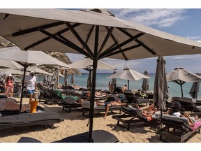 Visitors on sunbeds beneath parasols at Elia Beach, Mykonos, Greece, on Sunday, June 12, 2022. The Greek islands have seen a rise in the numbers of tourists visiting the country after two years of strict Covid-19 restrictions.