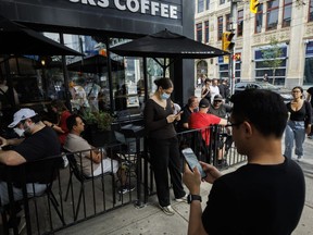 People use electronics outside a coffee shop in Toronto amid a countrywide Rogers outage, affecting many of the telecommunication company's services, Friday, July 8, 2022.