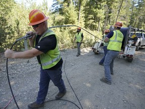 FILE - Carl Roath, left, a worker with the Mason County (Wash.) Public Utility District, pulls fiber optic cable off of a spool, as he works with a team to install broadband internet service to homes in a rural area surrounding Lake Christine near Belfair, Wash., on Aug. 4, 2021. Federal officials announced plans Thursday, July 28, 2022, to spend $401 million in grants and loans to expand the reach and improve the speed of internet for rural residents, tribes and businesses in 11 West and Central U.S. states.