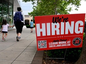 People walk past a "now hiring" sign posted outside of a restaurant in Arlington, Virginia.
