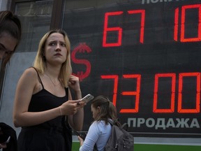 FILE - A woman walks past an exchange office screen showing the currency exchange rates of U.S. Dollar to Russian Rubles in St. Petersburg, Russia, July 5, 2022. The Russian central bank has slashed its key interest rate just a month after dropping it to where it was before sending troops into Ukraine, saying inflation is still easing partly as consumer demand falls. The bank on Friday, July 22 lowered its key rate by 1.5 percentage points, to 8%.