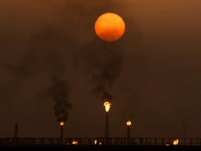 The sun sets as flare stacks burn off excess gas at an Iraqi oil field.
