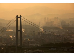 Smoke billows from an industrial complex beyond the Ulsan Harbor Bridge at dusk in Ulsan, South Korea, on Sunday, Aug. 4, 2019. Ulsan is known as Hyundai Town, an industrial powerhouse with the world's largest car-assembly plant, its third-biggest oil refinery and the giant shipyards. Since 2016, some 35,000 workers quit or lost their jobs at the city's shipyard, in a downturn as dramatic as it was sudden.